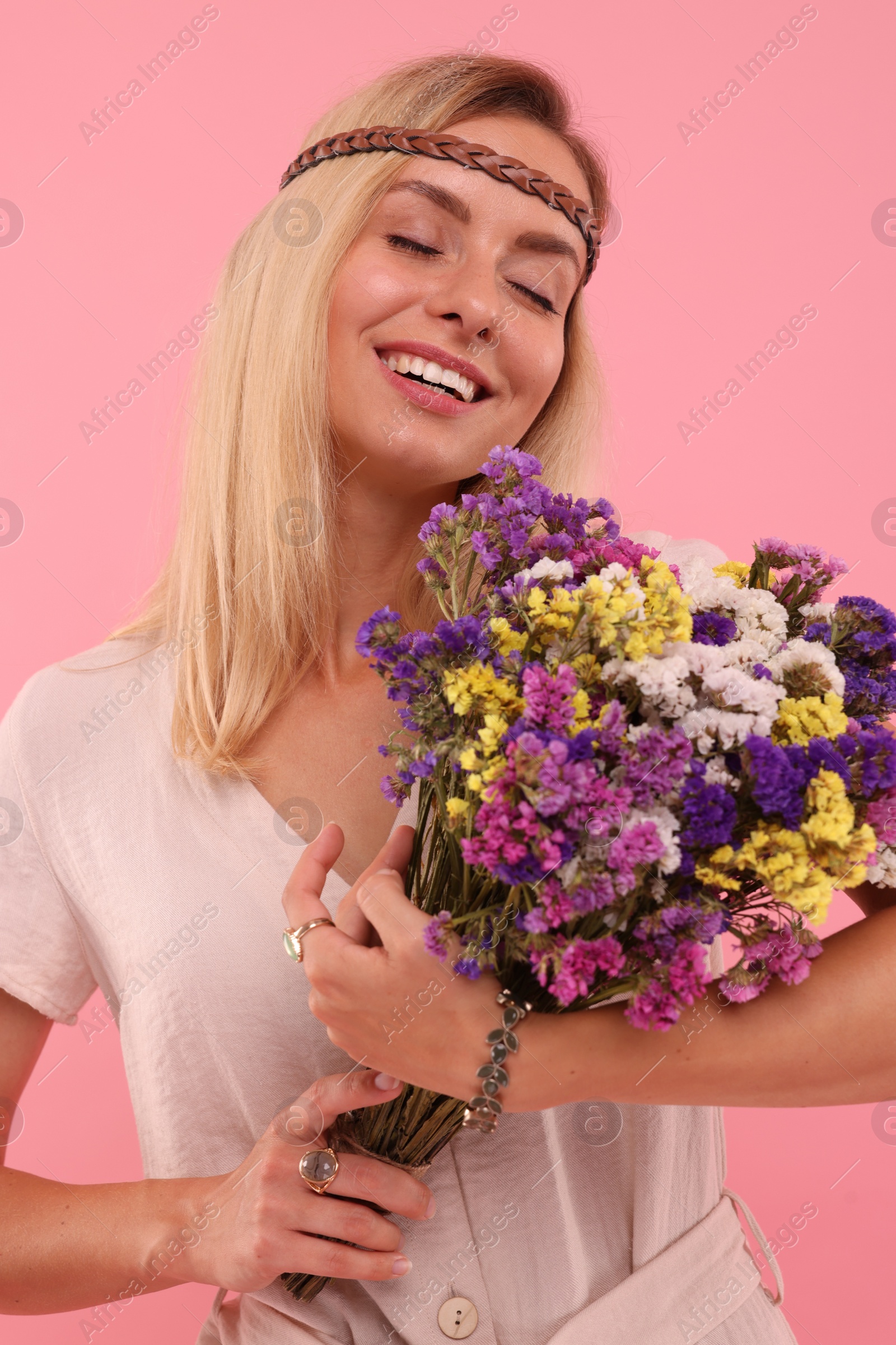 Photo of Portrait of smiling hippie woman with bouquet of flowers on pink background