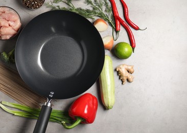 Empty iron wok surrounded by raw ingredients on grey table, flat lay. Space for text