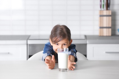 Photo of Cute little girl with glass of milk at table in kitchen