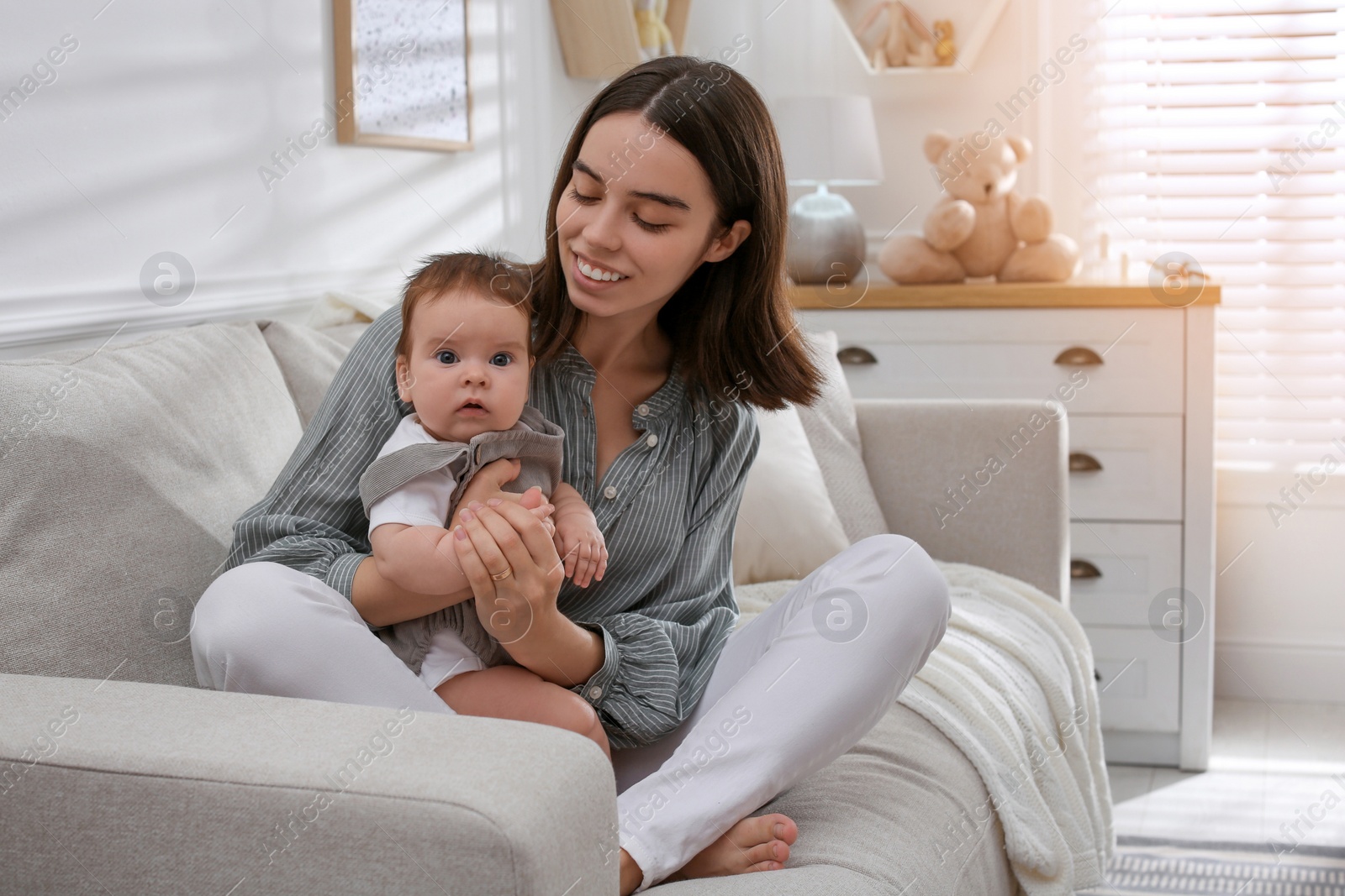 Photo of Young woman with her little baby on sofa at home