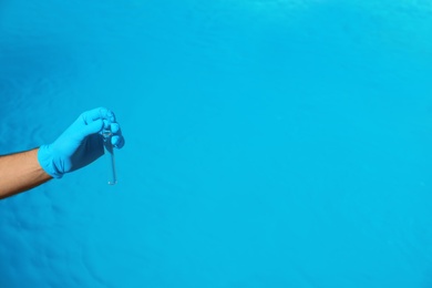 Man holding test tube with water against swimming pool on sunny day. Space for text