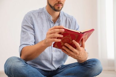 Photo of Muslim man reading Koran indoors, closeup view