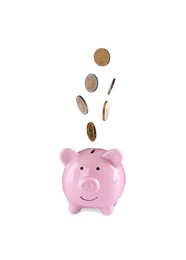 Different coins falling into cute piggy bank on white background