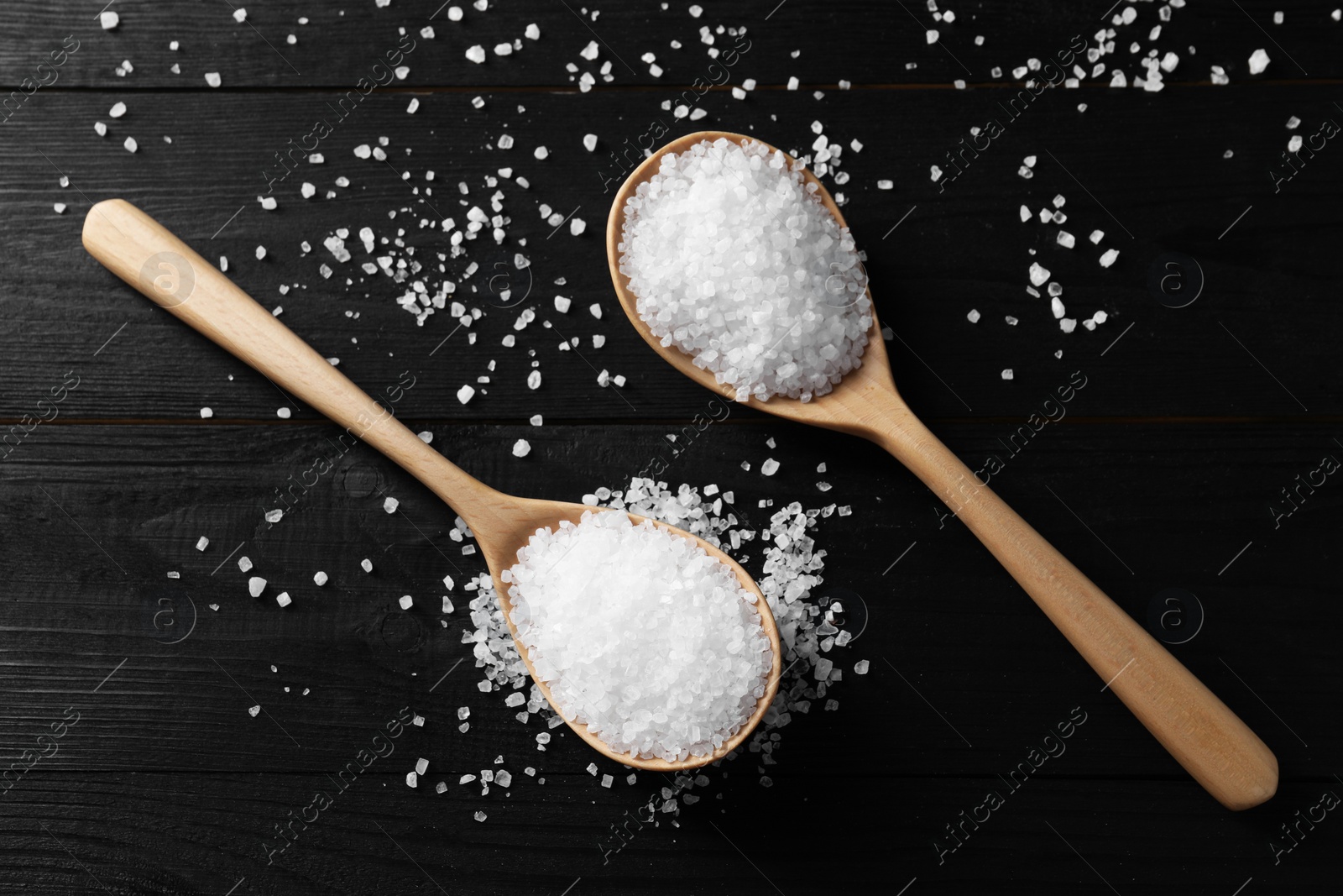 Photo of Organic salt in spoons on black wooden table, top view