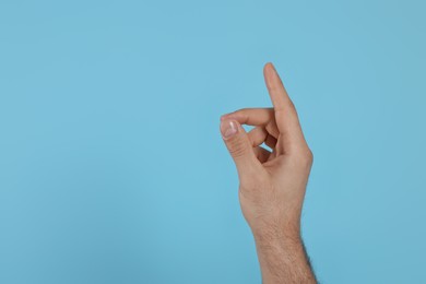 Man pointing at something on light blue background, closeup of hand. Space for text