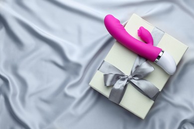 Photo of Gift box and pink vaginal vibrator on grey silk fabric, top view with space for text. Sex toy