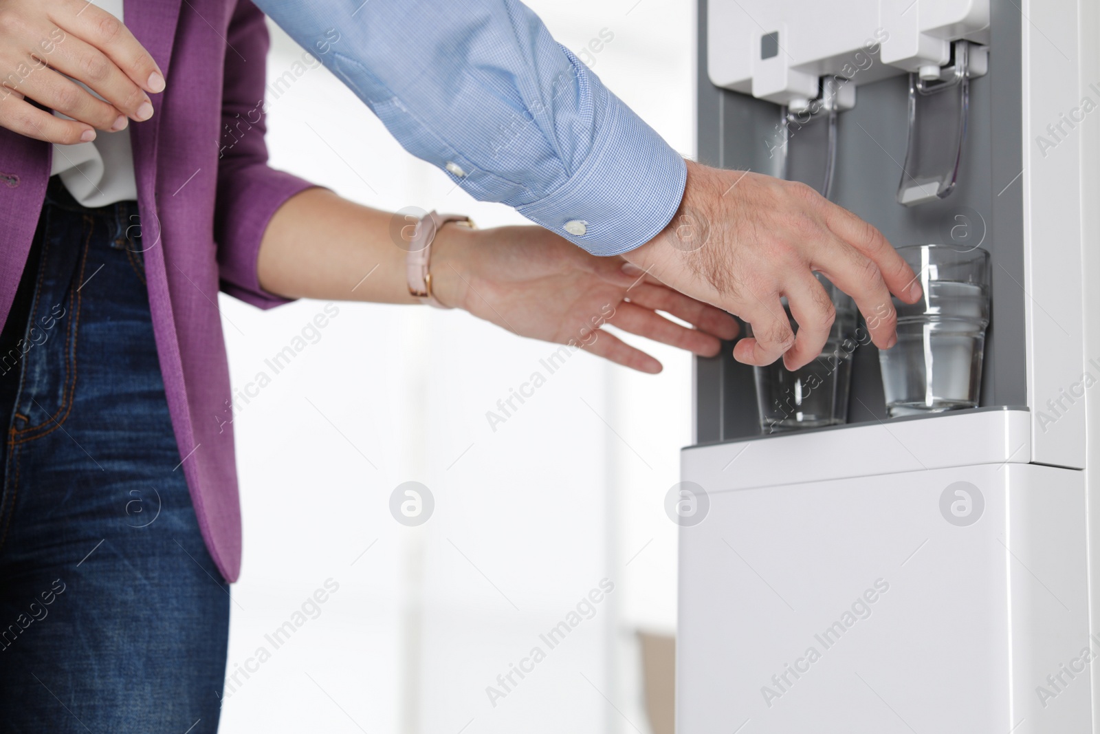 Photo of Employees taking glasses of water from cooler in office, closeup