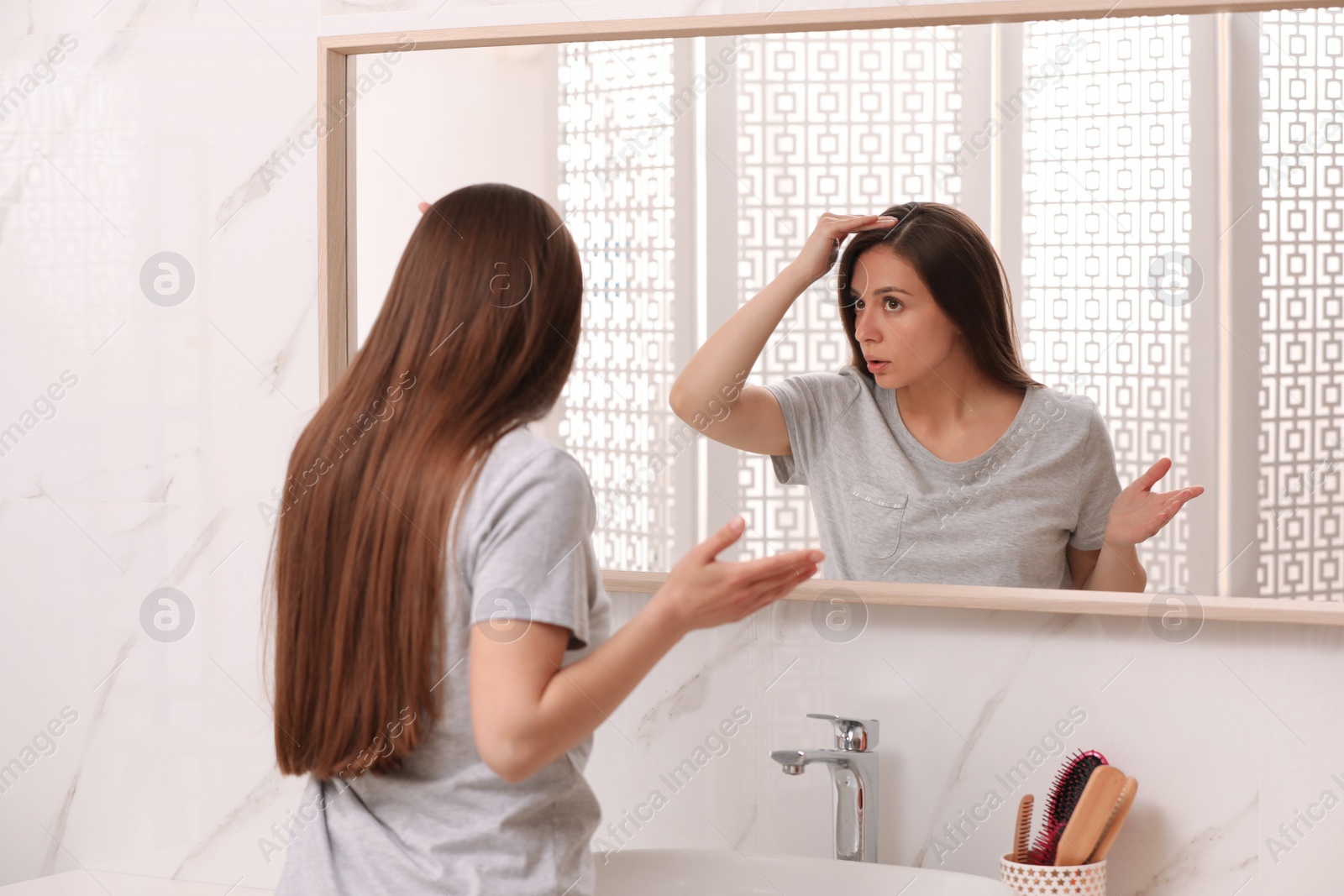 Photo of Young woman with hair loss problem looking near mirror in bathroom