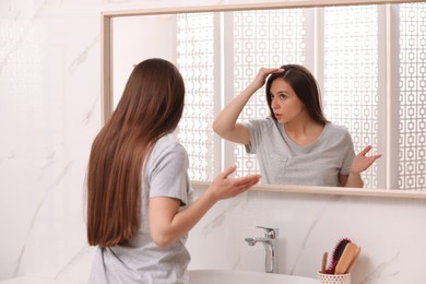 Photo of Young woman with hair loss problem looking near mirror in bathroom