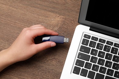 Photo of Woman attaching usb flash drive into laptop at wooden table, closeup