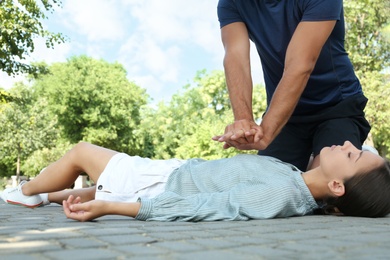 Photo of Man performing CPR on unconscious young woman outdoors. First aid