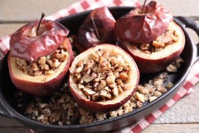 Photo of Tasty baked apples with nuts in baking dish on wooden table, closeup