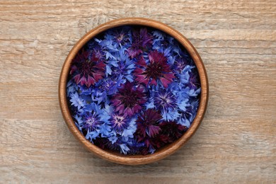 Photo of Beautiful colorful cornflowers in bowl on wooden table, top view