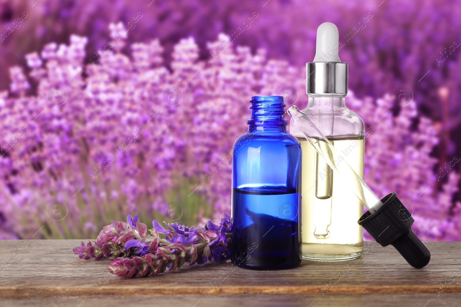 Image of Bottles of essential oil and sage flowers on wooden table against blurred background. Space for text