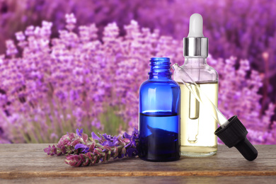 Bottles of essential oil and sage flowers on wooden table against blurred background. Space for text