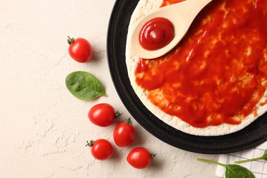 Photo of Pizza base smeared with sauce, tomatoes and basil on light textured table, flat lay