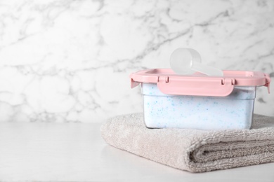 Photo of Closed container with detergent powder, towel and measuring spoon on table. Space for text