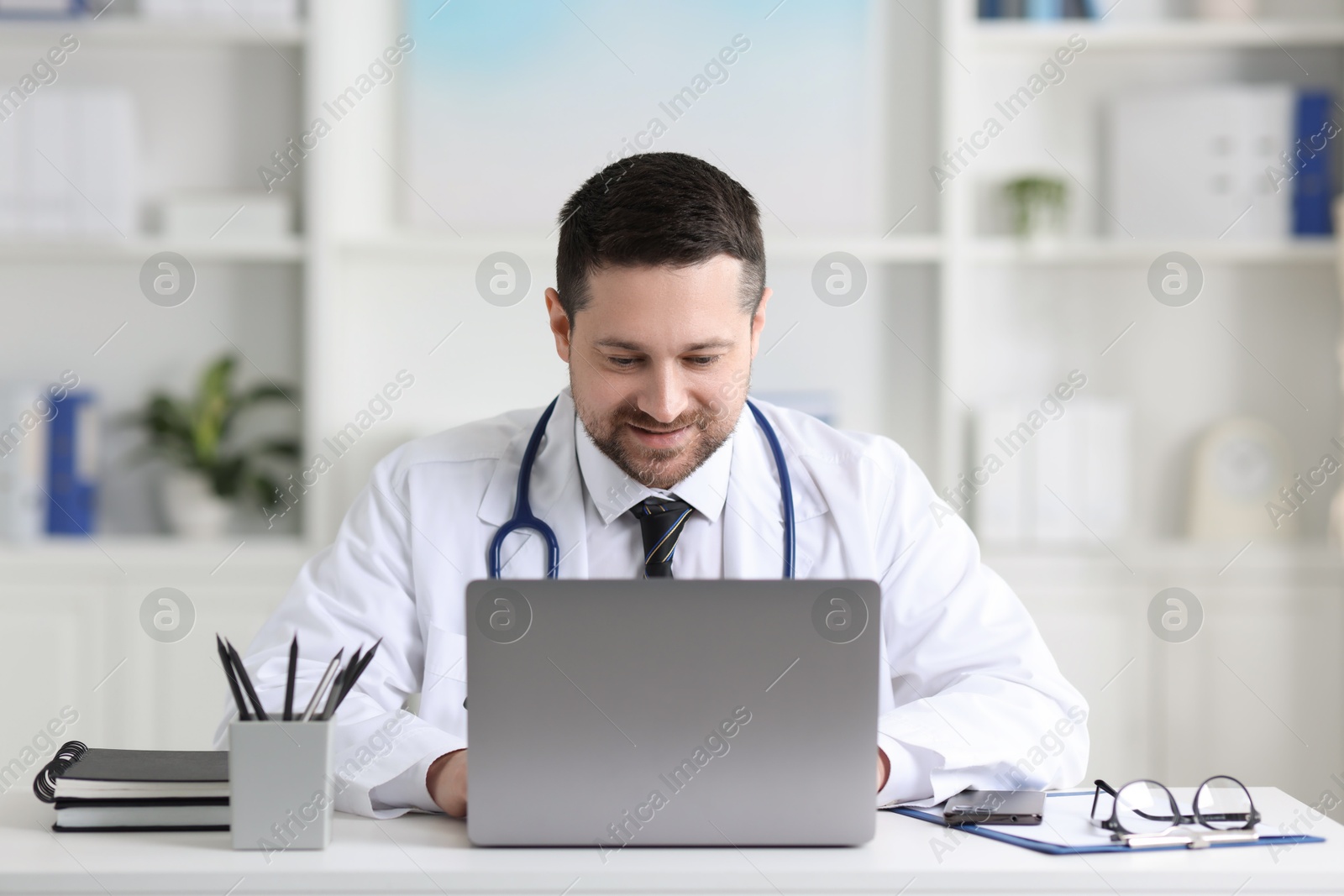 Photo of Doctor having online consultation via laptop at table in clinic