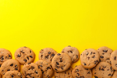 Photo of Many delicious chocolate chip cookies on yellow background, flat lay. Space for text