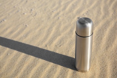 Metallic thermos with hot drink on sand, space for text