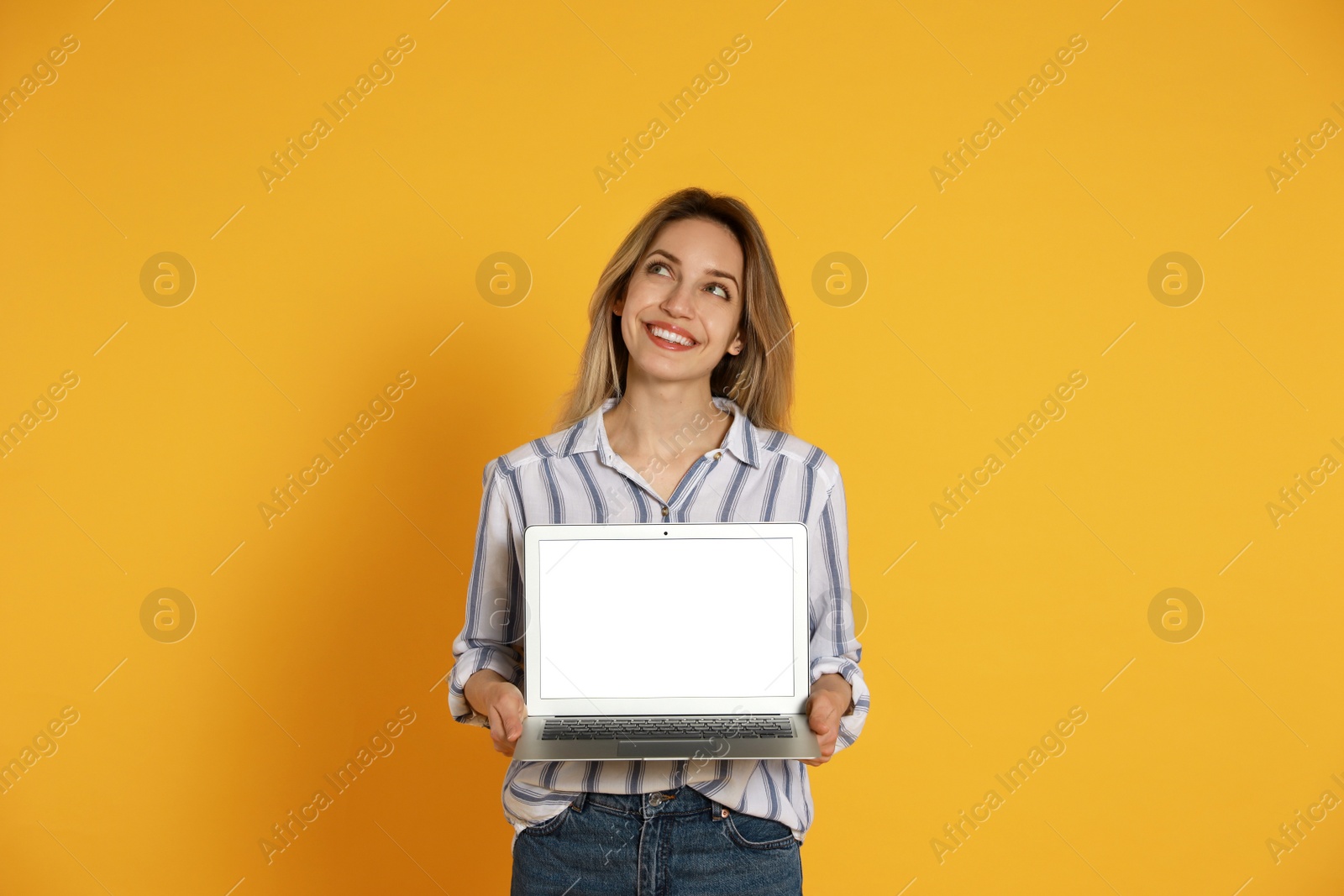 Photo of Young woman with modern laptop on yellow background