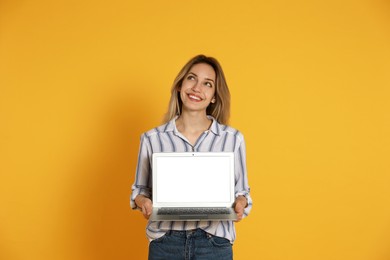 Photo of Young woman with modern laptop on yellow background