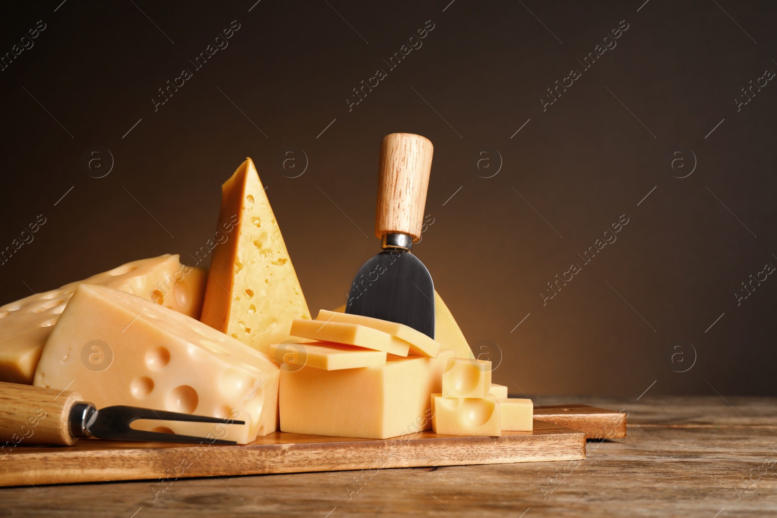 Photo of Different sorts of cheese, fork and knife on wooden table