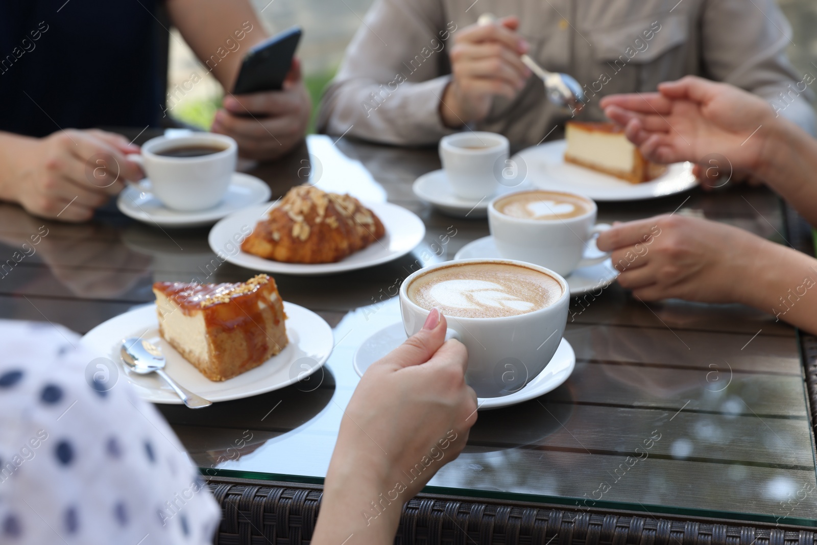 Photo of Friends drinking coffee at wooden table in outdoor cafe, closeup