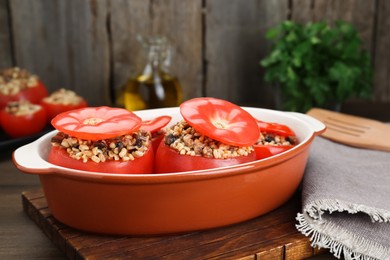 Photo of Delicious stuffed tomatoes with minced beef, bulgur and mushrooms in baking dish on wooden board