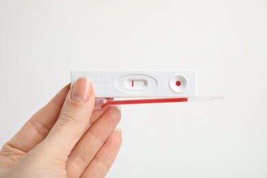 Photo of Woman holding disposable express test for hepatitis and pipette with blood on white background, closeup
