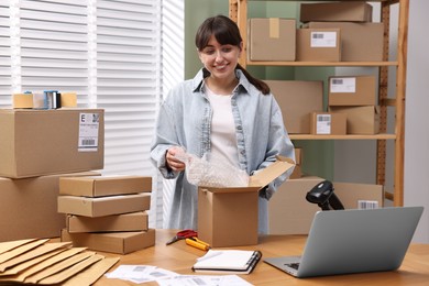 Post office worker packing parcel at wooden table indoors