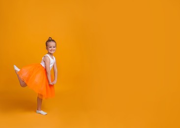 Photo of Cute little girl in tutu skirt dancing on orange background. space for text