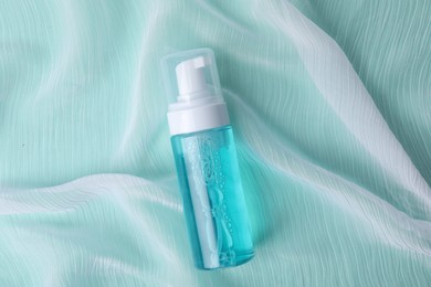 Photo of Bottle of face cleansing product on turquoise fabric, top view