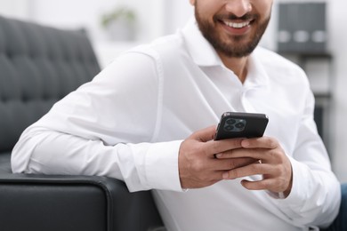 Young man using smartphone indoors, selective focus