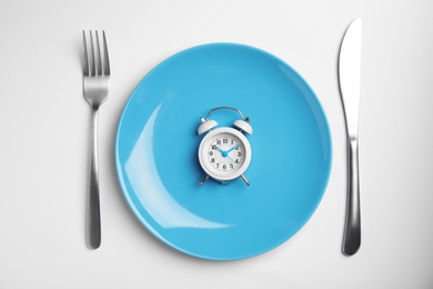 Alarm clock, plate and cutlery on white background, top view. Diet regime