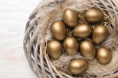 Photo of Many golden eggs in nest on white wooden table, top view