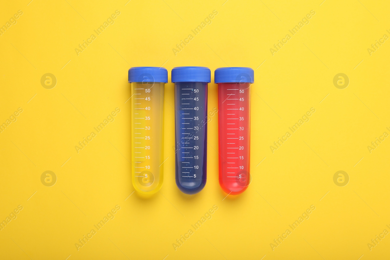 Photo of Test tubes with colorful liquids on yellow background, flat lay. Kids chemical experiment set