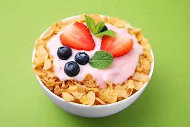 Photo of Delicious crispy cornflakes, yogurt and fresh berries in bowl on green background, closeup. Healthy breakfast