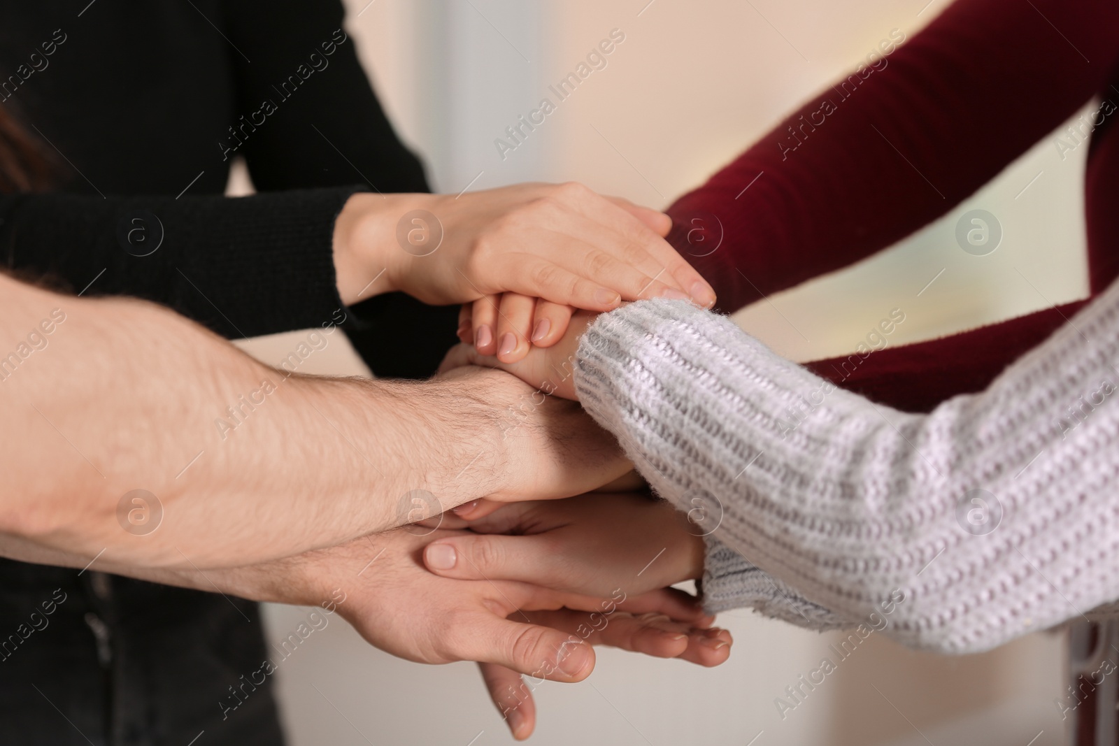 Photo of Young people putting their hands together on blurred background, closeup