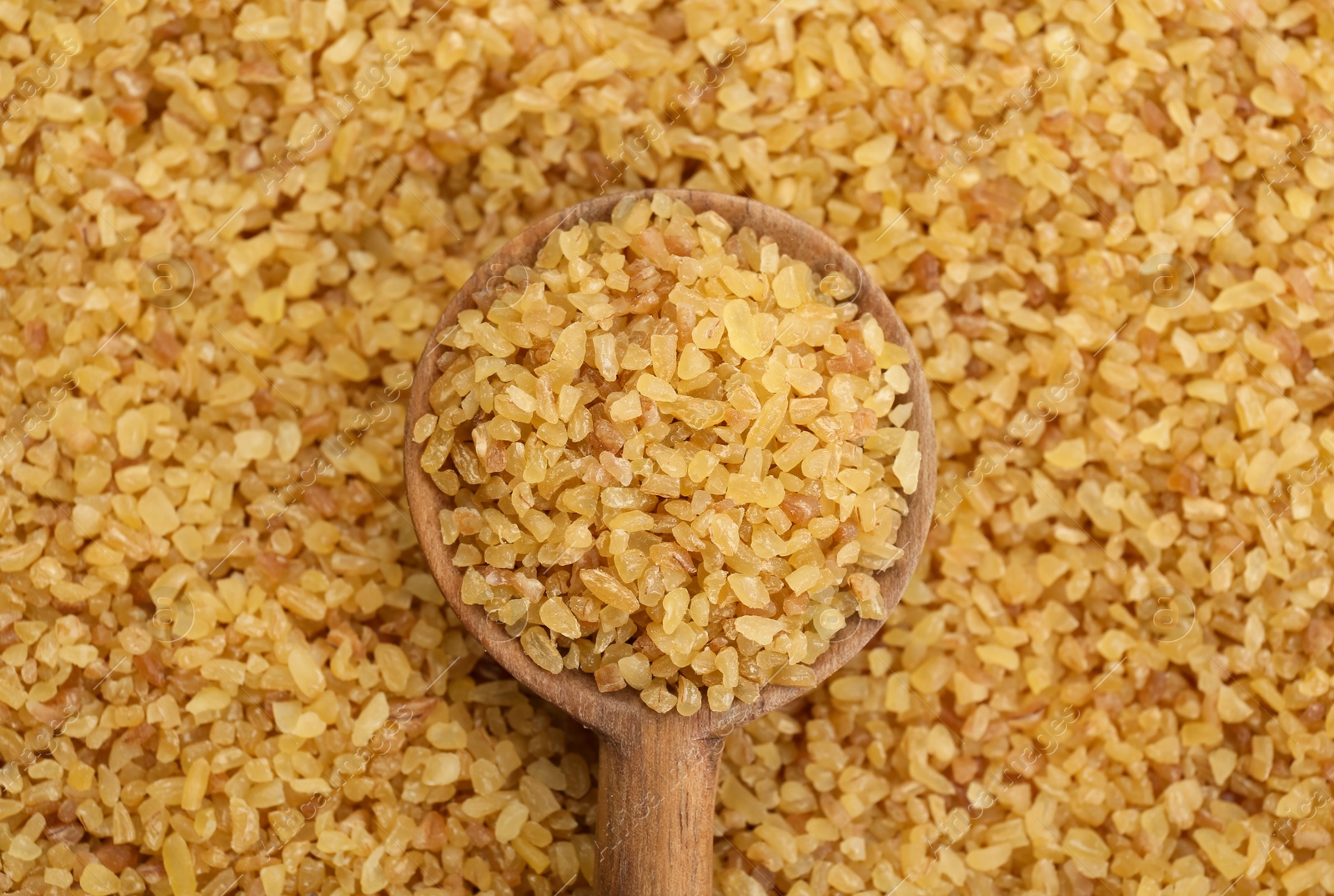 Photo of Wooden spoon on pile of uncooked bulgur, top view