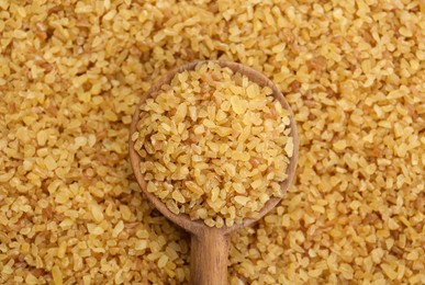 Wooden spoon on pile of uncooked bulgur, top view