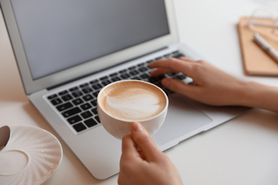 Photo of Young blogger with cup of coffee working at table in cafe, closeup