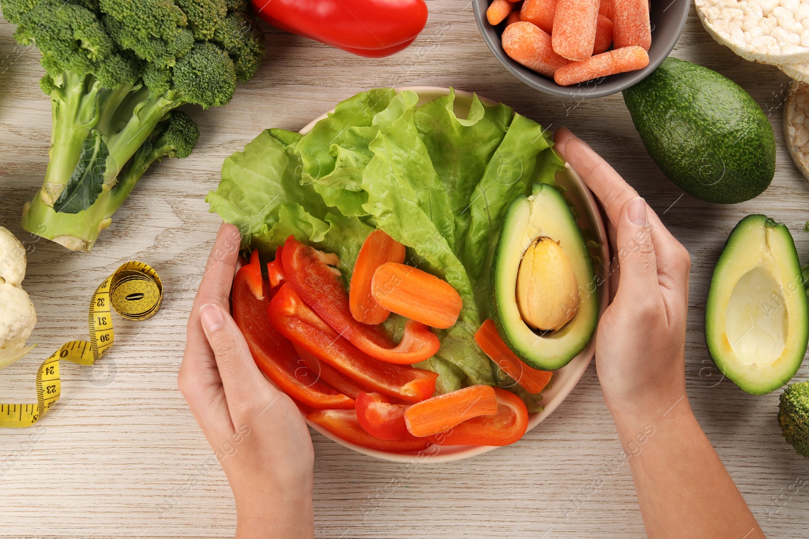 Photo of Healthy diet. Woman with fresh vegetables and measuring tape at light wooden table, top view