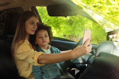 Photo of Mother with little daughter driving car and taking selfie. Child in danger