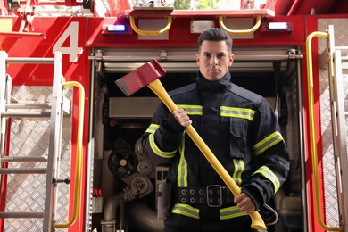 Portrait of firefighter in uniform with axe near fire truck outdoors