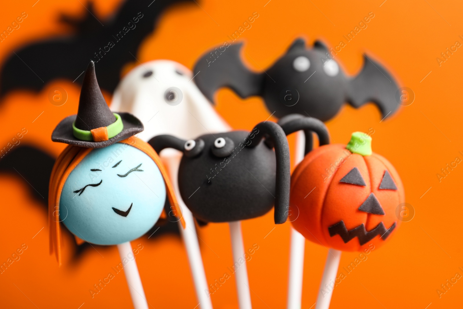 Photo of Delicious Halloween themed cake pops on orange background, closeup