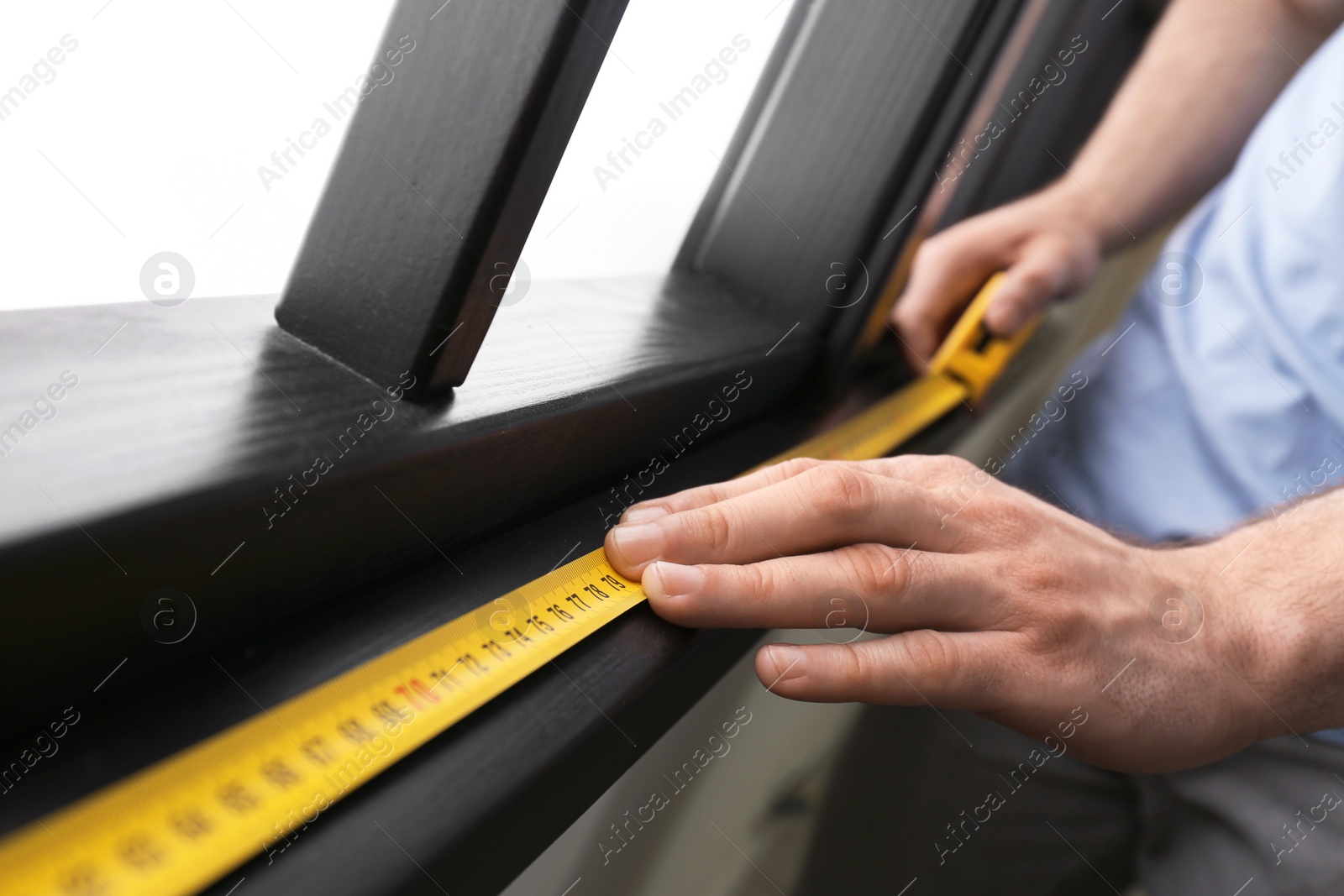 Photo of Man measuring wooden window frame indoors, closeup. Construction tool
