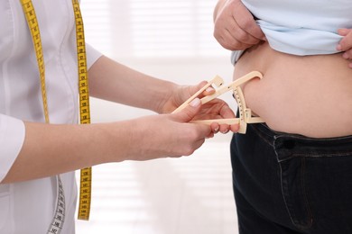 Photo of Nutritionist measuring overweight woman's body fat layer with caliper in clinic, closeup