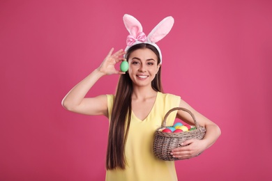 Photo of Beautiful woman in bunny ears headband with Easter eggs on color background