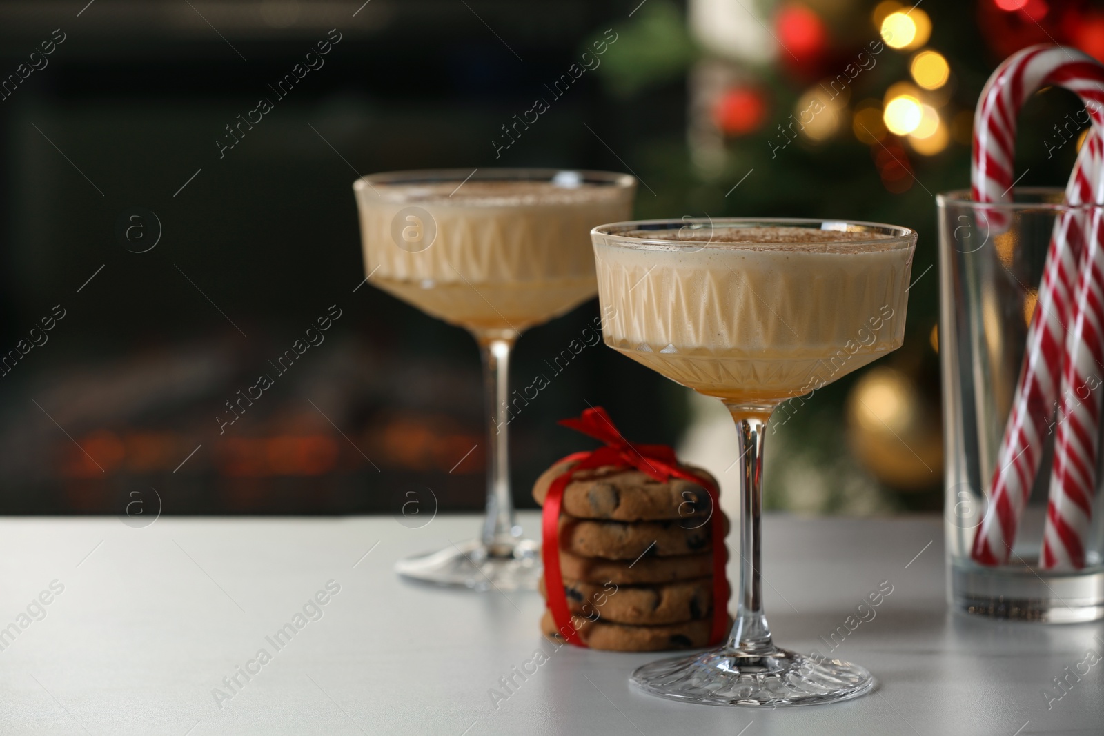 Photo of Tasty eggnog, cookies and candy canes on white marble table against blurred festive lights. Space for text